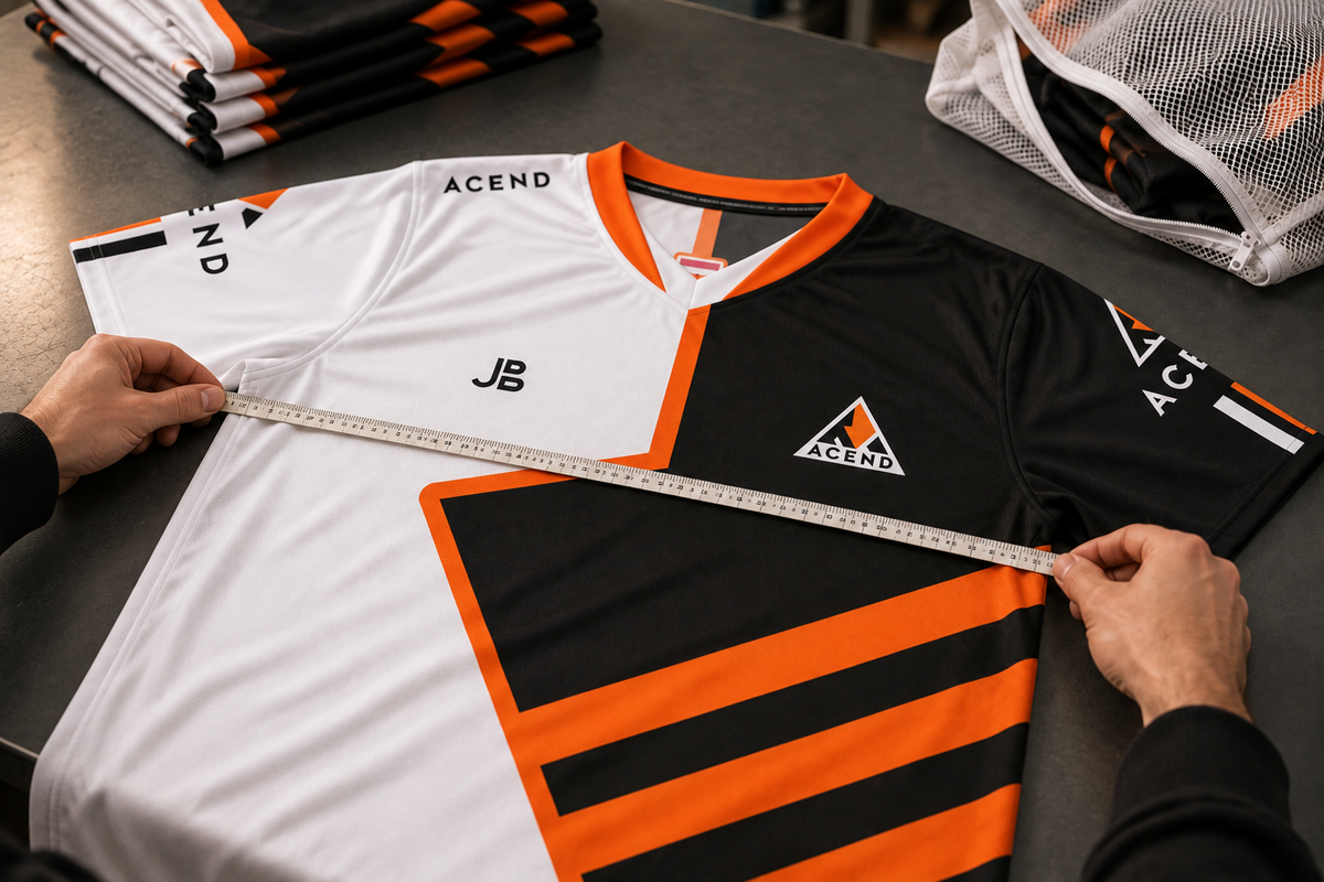 Illustrative image: the black, white and orange ACEND 2024 jersey is laid flat and measured with a tape measure. Folded teamwear and a mesh laundry bag sit beside it.